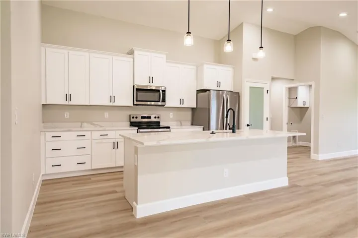 Kitchen featuring white cabinets, appliances with stainless steel finishes, a center island with sink, and hanging light fixtures