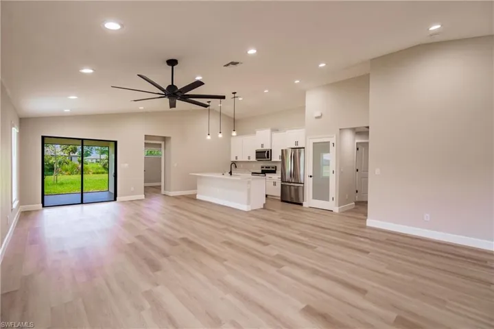 Unfurnished living room featuring sink, vaulted ceiling, light hardwood / wood-style floors, and ceiling fan