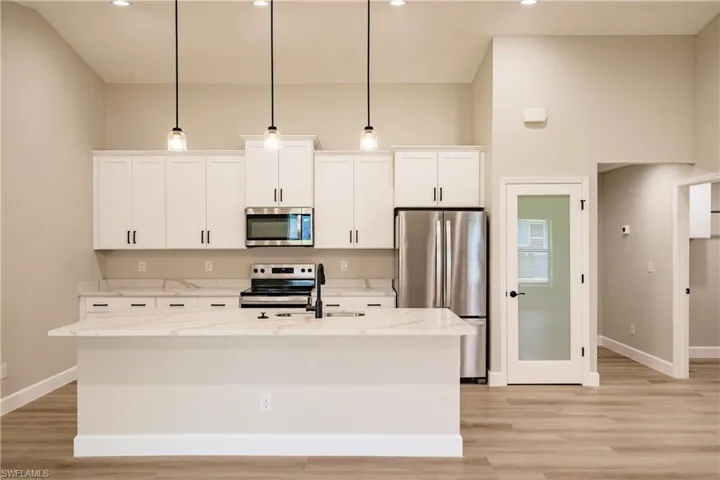 Kitchen featuring light stone counters, appliances with stainless steel finishes, an island with sink, and hanging light fixtures