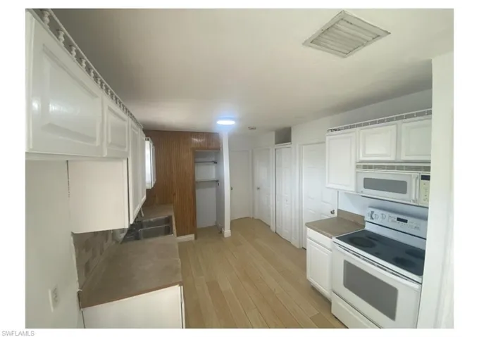 Kitchen with white appliances, white cabinets, sink, and light hardwood / wood-style flooring