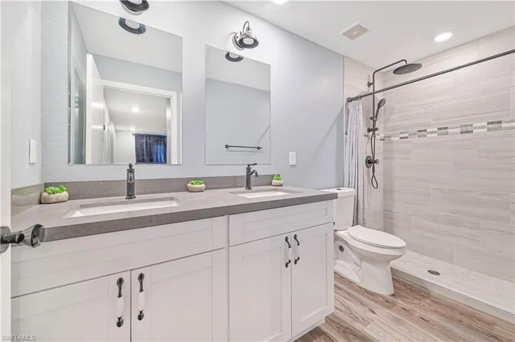 Bathroom with curtained shower, hardwood / wood-style flooring, double vanity, and toilet