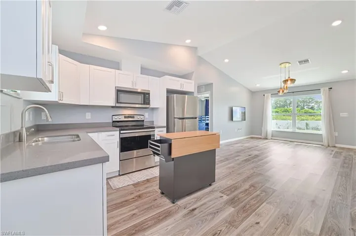 Kitchen with vaulted ceiling, light wood-type flooring, sink, white cabinetry, and appliances with stainless steel finishes