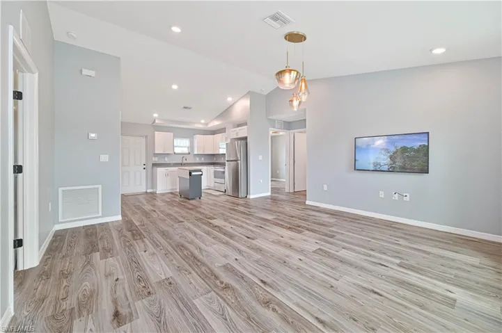 Unfurnished living room featuring sink, vaulted ceiling, and light hardwood / wood-style flooring