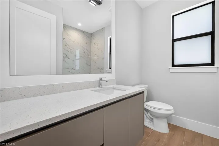 Bathroom featuring a contemporary floating vanity with an integrated sink, a speckled quartz countertop, a mirrored wall, and wood-finish tile flooring