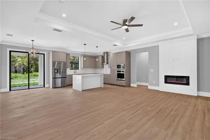 Open-concept interior featuring wood-finish flooring, a modern kitchen with stainless steel appliances, a center island, and a built-in electric fireplace