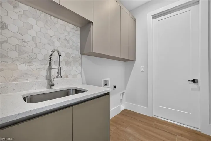 Laundry room featuring a stainless steel sink, solid surface countertop, and hexagon tile backsplash