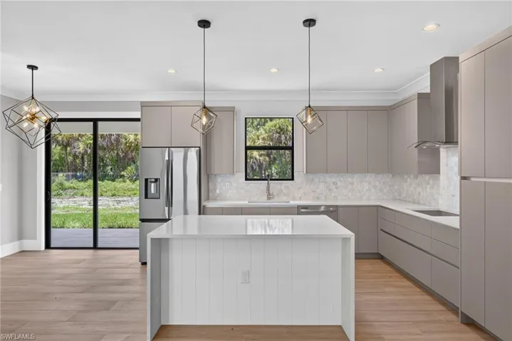 Modern kitchen featuring an expansive island with a waterfall countertop, contemporary pendant lighting, stainless steel appliances, and wood-finish flooring