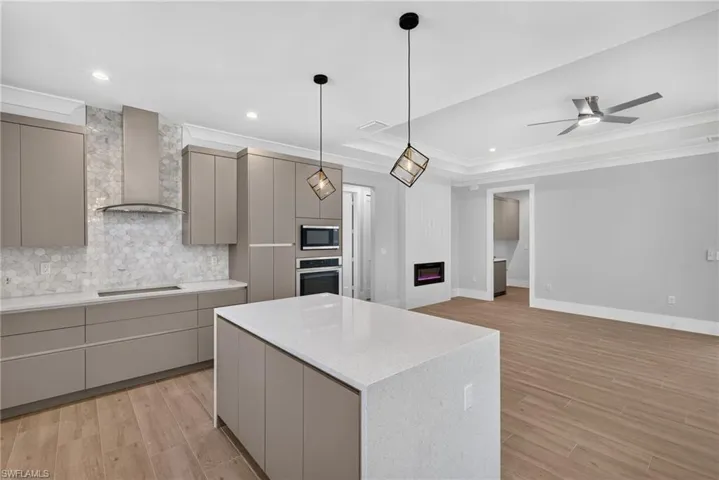 Modern kitchen featuring an expansive island with a light-toned countertop, contemporary flat-panel cabinetry, a hexagon tile backsplash, stainless steel appliances, and wood-finish flooring
