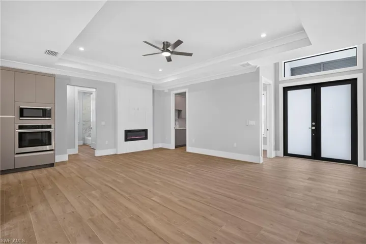 Spacious room featuring wood-finish flooring, a contemporary electric fireplace with white shiplap surround, and built-in stainless steel appliances
