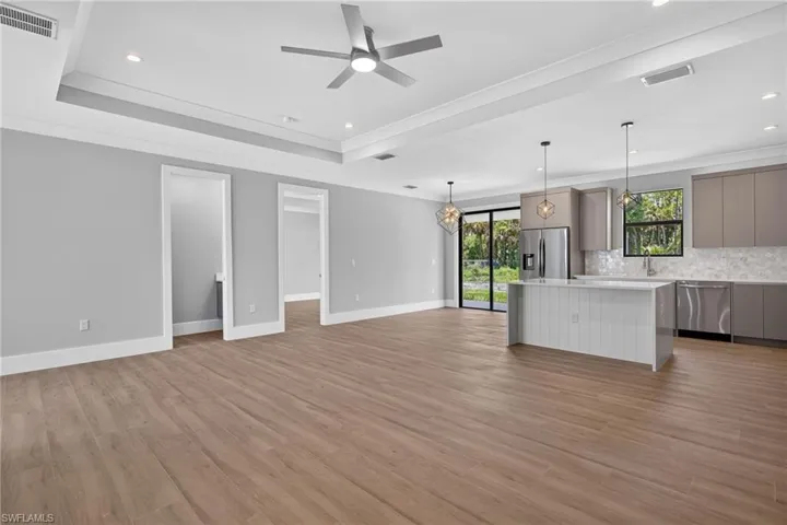 Spacious open-concept living area featuring wood-finish flooring, a tray ceiling with recessed lighting and a ceiling fan, and access to the outdoors via a sliding glass door