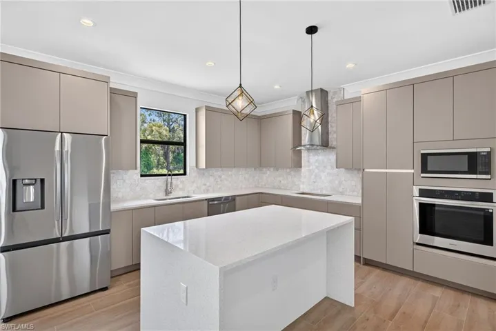 Modern kitchen featuring a central island with a solid surface countertop, stainless steel appliances, contemporary cabinetry, a geometric backsplash, and integrated recessed lighting