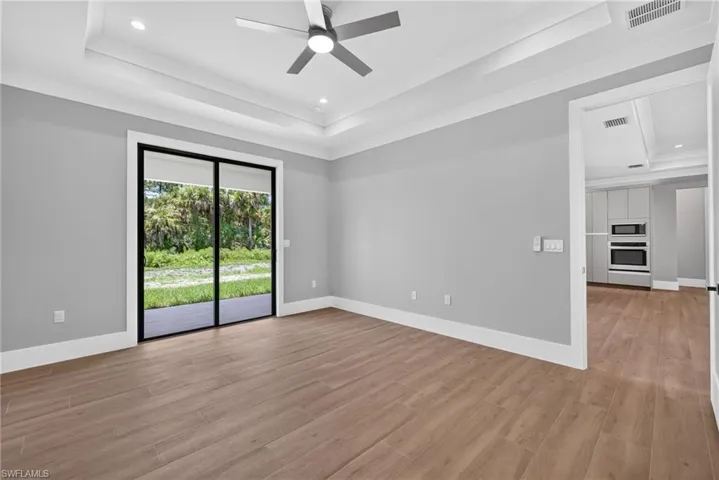 Spacious interior room featuring wood-finish flooring, a tray ceiling with recessed lighting, and a ceiling fan