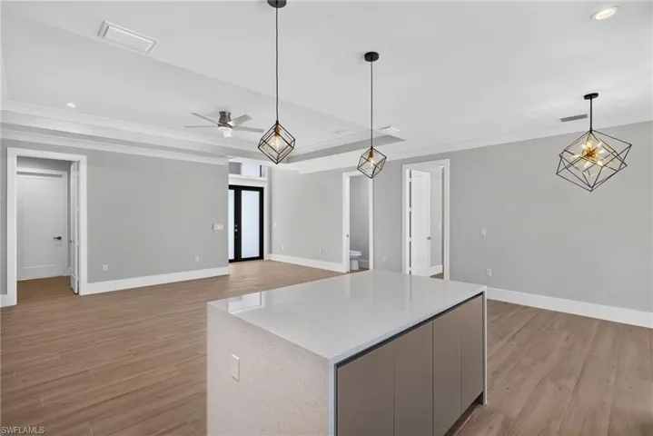 Spacious interior featuring a large kitchen island with a light-toned countertop, wood-finish flooring, recessed lighting, and modern geometric pendant lights