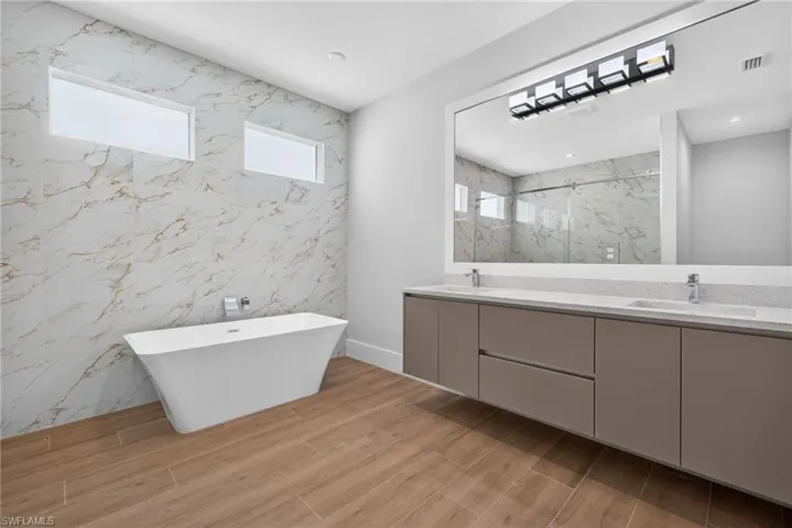 Modern bathroom featuring a freestanding tub, large format marble-look wall tile, dual vanity with undermount sinks, and wood-finish flooring