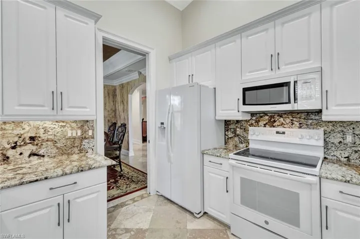 Kitchen with white appliances, white cabinets, crown molding, light stone countertops, and backsplash