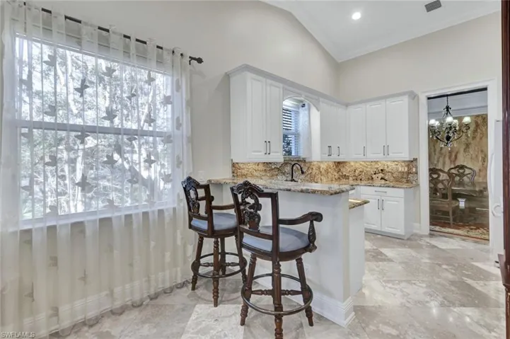 Kitchen featuring vaulted ceiling, white cabinets, light stone counters, a chandelier, and a breakfast bar area