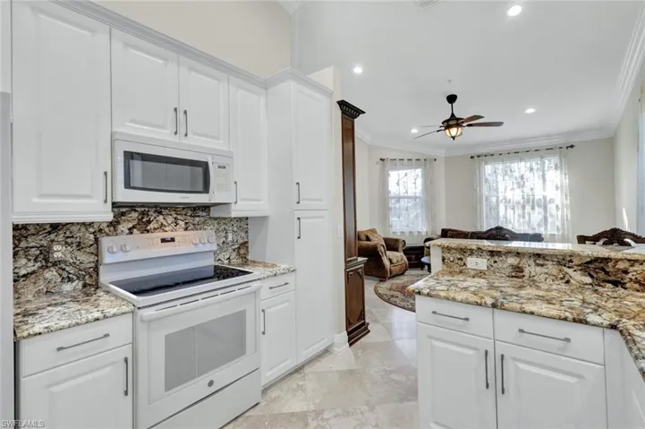 Kitchen featuring white appliances, open floor plan, crown molding, white cabinets, and light stone counters