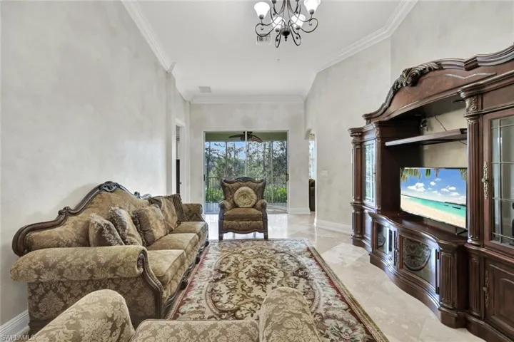 Living room with light marble finish floors, crown molding, and a chandelier