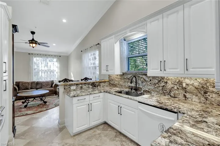 Kitchen with crown molding, white cabinets, vaulted ceiling, white dishwasher, and open floor plan