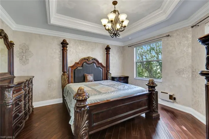 Bedroom with dark wood-style flooring, a chandelier, a raised ceiling, and ornamental molding