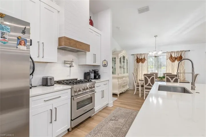 Kitchen featuring appliances with stainless steel finishes, white cabinetry, a chandelier, decorative light fixtures, and light stone counters