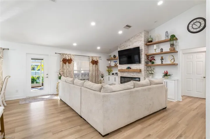 Living room featuring a fireplace, light wood-type flooring, recessed lighting, and high vaulted ceiling