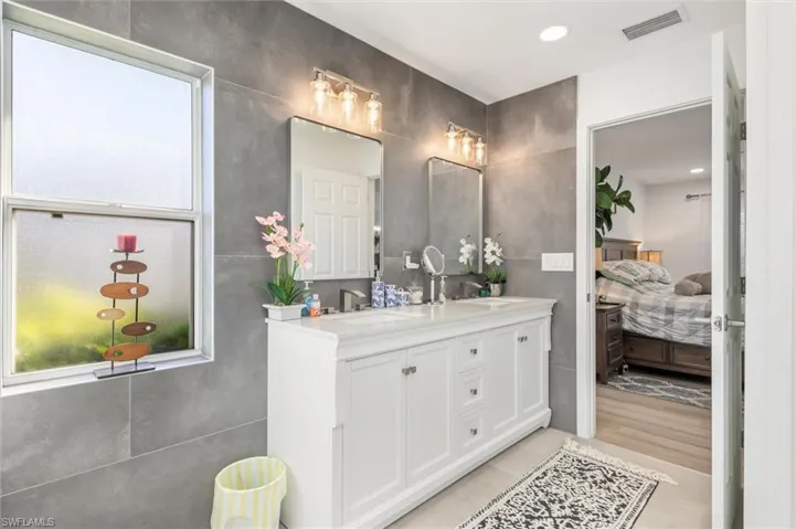 Full bathroom with double vanity, connected bathroom, tile walls, and recessed lighting