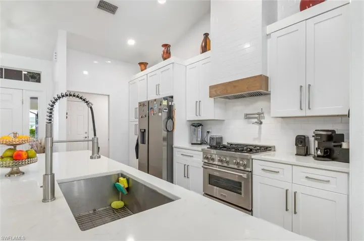 Kitchen featuring stainless steel appliances, white cabinets, light stone counters, premium range hood, and recessed lighting