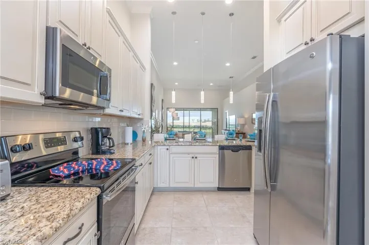 Kitchen featuring stainless steel appliances, decorative light fixtures, light stone counters, backsplash, and white cabinetry
