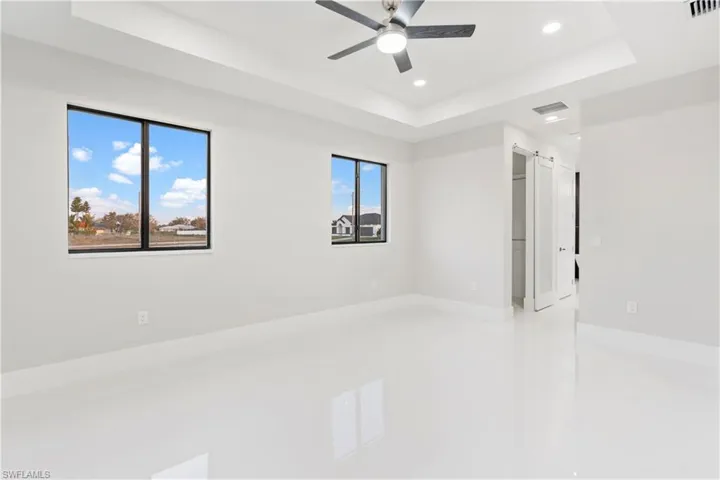 Spare room with a barn door, a wealth of natural light, ceiling fan, and a tray ceiling