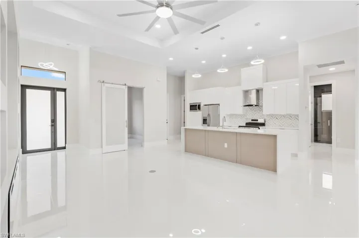 Kitchen with appliances with stainless steel finishes, white cabinets, a large island, a barn door, and wall chimney range hood