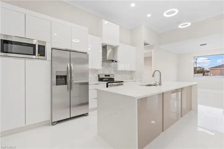 Kitchen with decorative light fixtures, white cabinetry, sink, stainless steel appliances, and wall chimney range hood