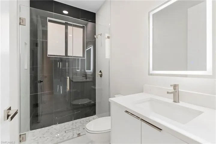 Bathroom featuring a shower with door, vanity, and toilet