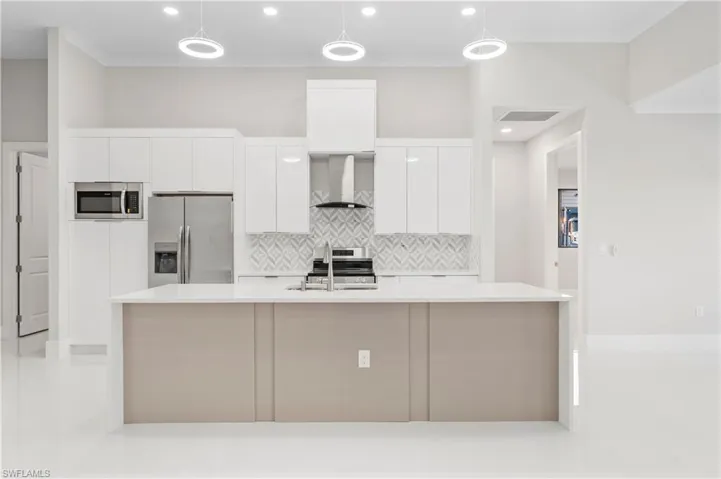 Kitchen with sink, white cabinetry, decorative light fixtures, appliances with stainless steel finishes, and wall chimney range hood