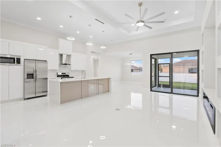 Kitchen featuring appliances with stainless steel finishes, a tray ceiling, white cabinets, and wall chimney exhaust hood