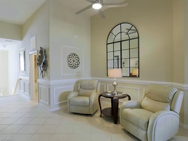 Sitting room featuring a decorative wall, light tile patterned flooring, ceiling fan, and a wainscoted wall