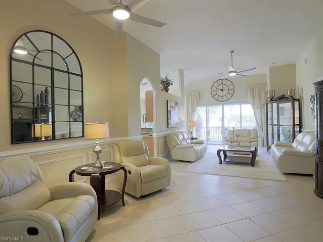 Living room featuring ceiling fan, light tile patterned floors, lofted ceiling, and arched walkways