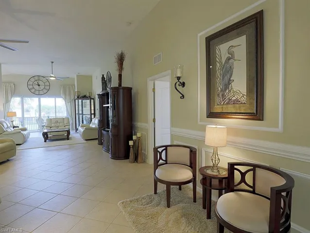 Living area featuring lofted ceiling, a wainscoted wall, light tile patterned floors, and a ceiling fan
