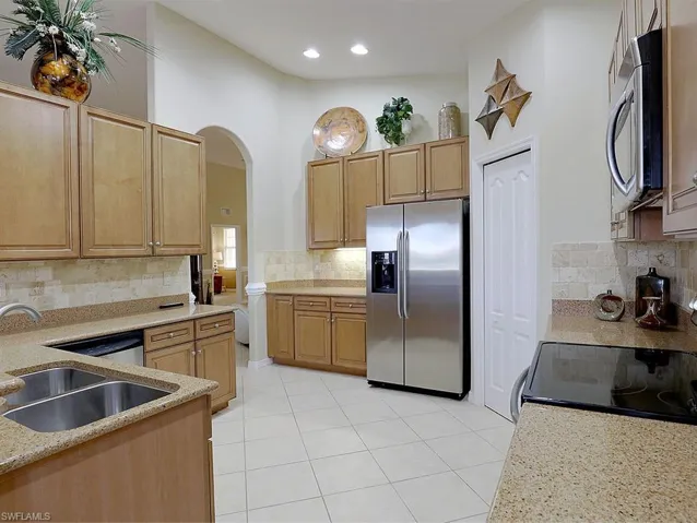 Kitchen with stainless steel appliances, light stone countertops, light tile patterned floors, and backsplash