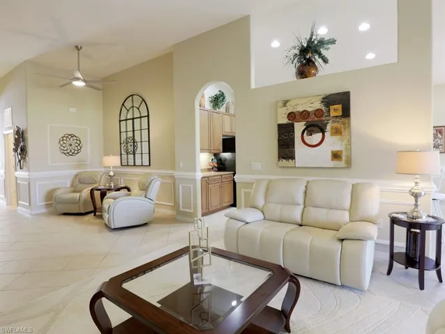 Living area featuring a decorative wall, wainscoting, ceiling fan, light tile patterned floors, and a high ceiling