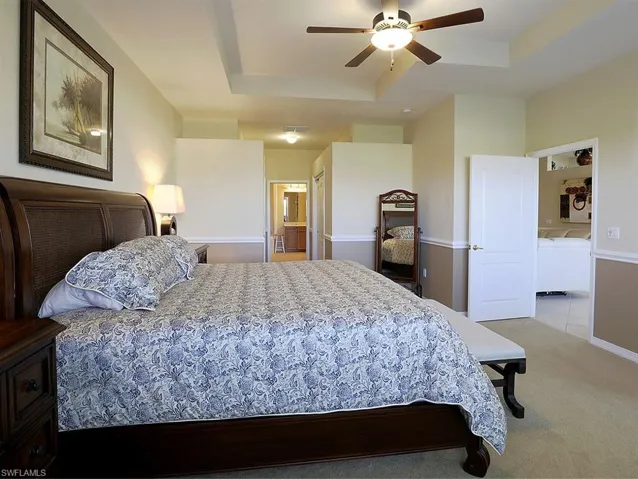 Bedroom featuring a tray ceiling, light carpet, ensuite bathroom, washing machine and clothes dryer, and ceiling fan