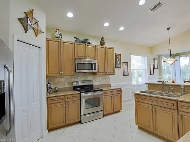 Kitchen with stainless steel appliances, decorative light fixtures, light tile patterned floors, decorative backsplash, and wood finish cabinetry