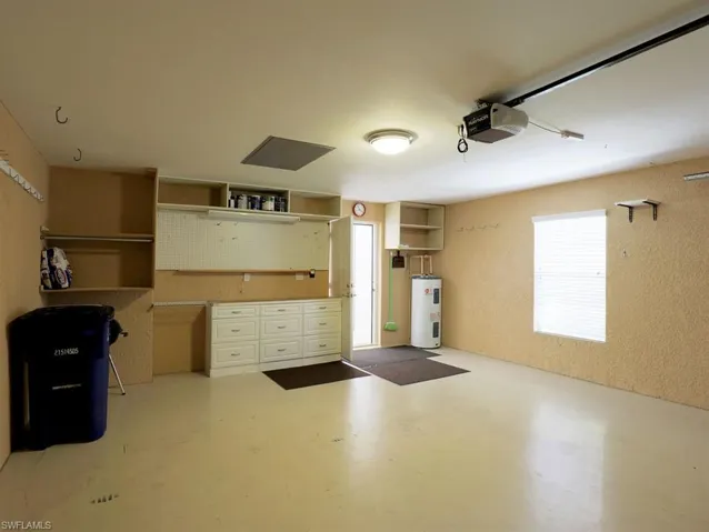Garage featuring water heater, a garage door opener, and a textured wall