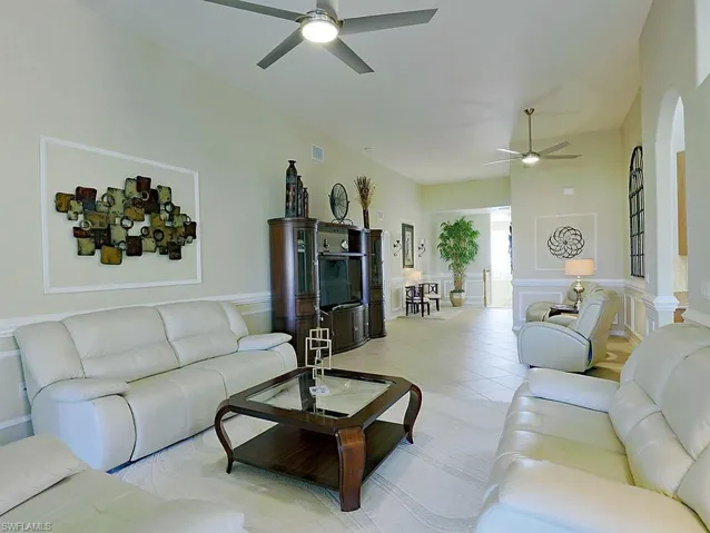 Living room with ceiling fan, light tile patterned floors, a wainscoted wall, and a decorative wall