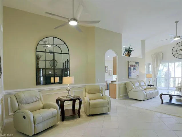 Living room featuring ceiling fan, arched walkways, lofted ceiling, wainscoting, and a decorative wall