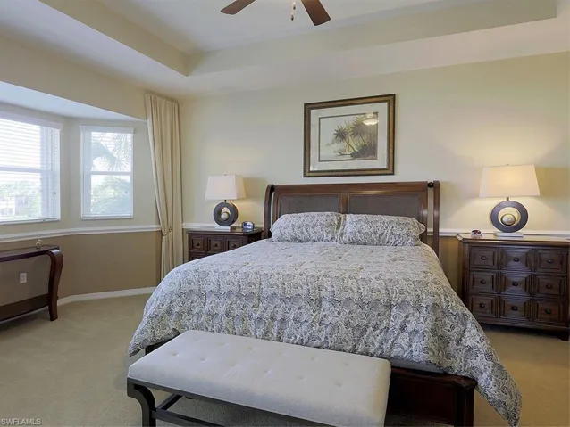 Bedroom with light colored carpet, ceiling fan, and a raised ceiling