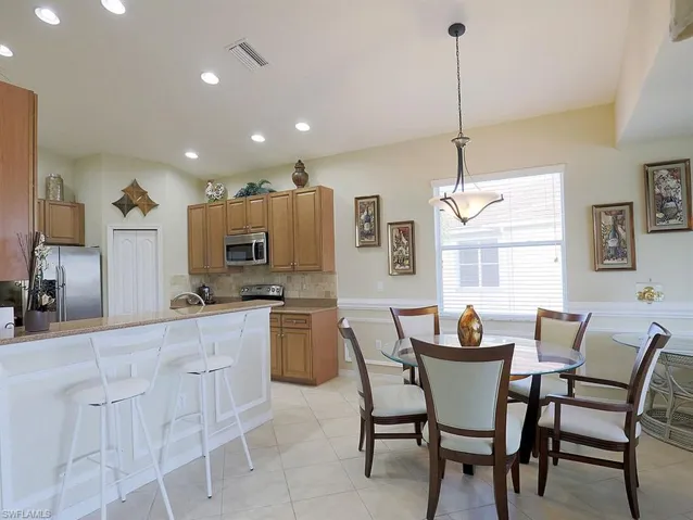 Kitchen featuring a kitchen breakfast bar, stainless steel appliances, wood finish cabinets, decorative backsplash, and decorative light fixtures
