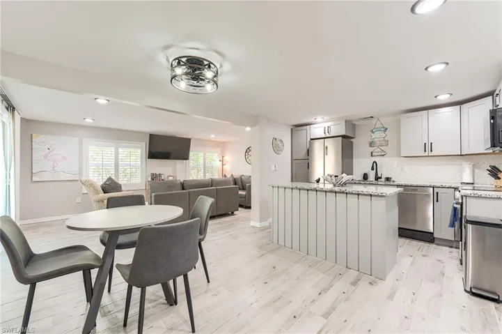 1st Floor Kitchen featuring recessed lighting, a kitchen island, light stone countertops, open floor plan, and tasteful backsplash- Virtually Edited Image