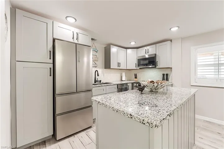 1st Floor Kitchen featuring stainless steel appliances, light stone counters, a center island, tasteful backsplash, and light wood-style flooring- Virtually Edited Image