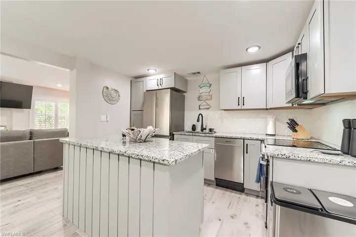 1st Floor Kitchen with a kitchen island, light stone countertops, tasteful backsplash, stainless steel appliances, and open floor plan- Virtually Edited Image